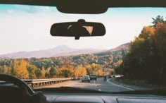 the view from inside a car looking at mountains, trees and cars on the road