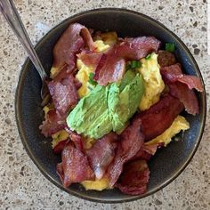 a black bowl filled with eggs, bacon and guacamole on top of a table