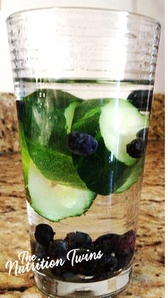 a glass filled with cucumbers and blueberries on top of a countertop