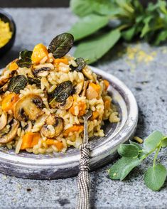 a plate filled with pasta and vegetables on top of a table next to some herbs