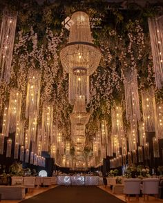 a large chandelier hanging from the ceiling in front of a stage with flowers and greenery