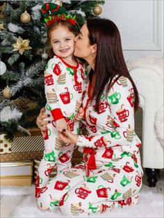 a mother and daughter kissing in front of a christmas tree wearing matching pajama's