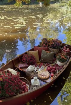 a boat filled with lots of flowers sitting on top of a river next to a forest