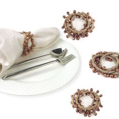 a white plate topped with silverware next to napkins and rings covered in beads