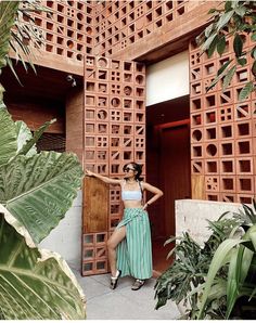 a woman standing in front of a wooden door with plants around her and wearing a skirt