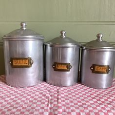 three metal canisters sitting on top of a checkered tablecloth covered table