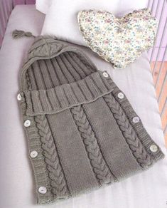 two knitted sweaters and a heart shaped pillow on top of a white bed