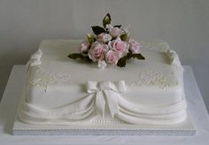 a white cake with pink roses on top and ribbon around the edges, sitting on a table