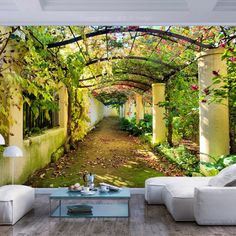 a living room filled with white furniture and walls covered in green trees, bushes and flowers