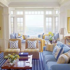 a living room filled with lots of furniture next to a large window covered in blue and yellow pillows