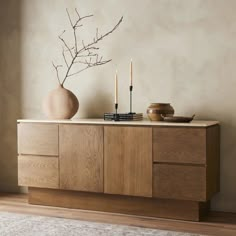 a vase and some candles on a wooden cabinet next to a rug in a room