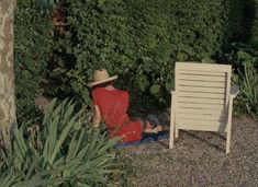 a woman sitting on the ground next to a chair in front of some trees and bushes