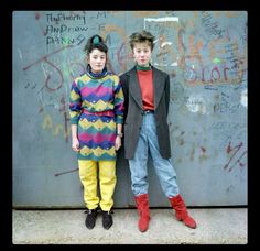 two young boys standing next to each other in front of a wall with graffiti on it