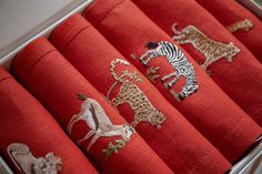 red fabric with embroidered animals and zebras in a white box on a table top