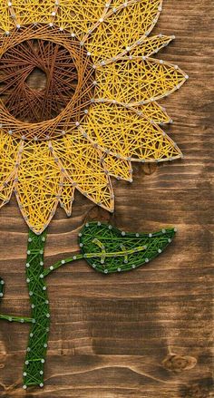 the string art sunflower is made out of yellow yarn and green leaves on a wooden surface