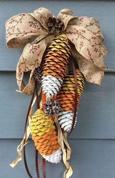 a wreath made out of pine cones hanging on the side of a building with ribbon