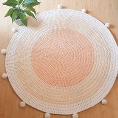 a round rug with pom - poms on the floor next to a potted plant