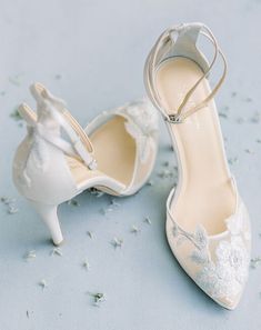 two pairs of white wedding shoes on a blue surface with flowers and petals scattered around them