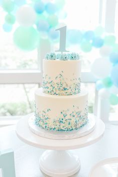 a white cake with blue sprinkles and a number one on top sitting on a table