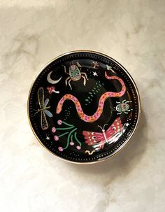 a black and pink dragon plate on a white counter top with stars, moths, and flowers