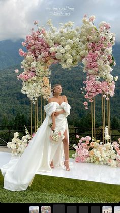 a woman in a white dress standing next to a flower covered arch with flowers on it