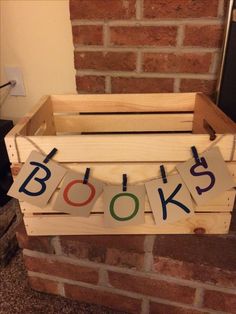 a wooden crate with the word books spelled in multicolored letters on it, sitting next to a brick wall