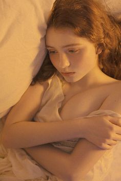 a young woman laying in bed with her arms folded over her chest and looking at the camera