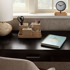 a desk with a clock, pen and pencil holder on it next to a window