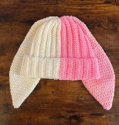 a pink and white knitted hat sitting on top of a wooden table