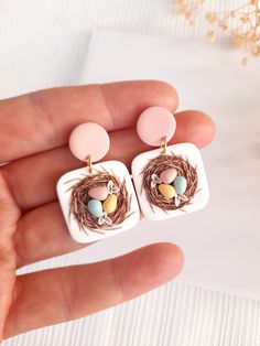 a hand holding two small bird's nest earrings with eggs in the nest on top