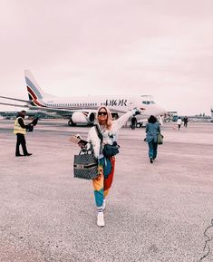 a woman standing in front of an airplane on the tarmac with her hand up