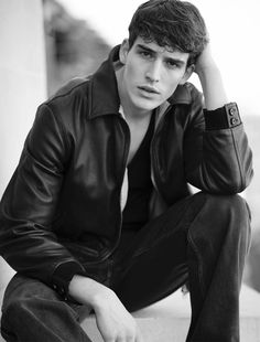 a young man sitting on the ground wearing a leather jacket