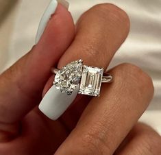 a woman's hand holding an engagement ring with two stones on it and a white manicure