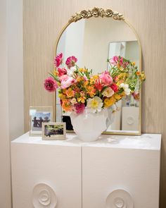 a vase filled with flowers sitting on top of a white dresser next to a mirror