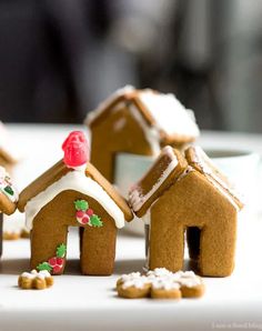 small gingerbread houses with frosting and holly decorations on the outside, sitting on a table