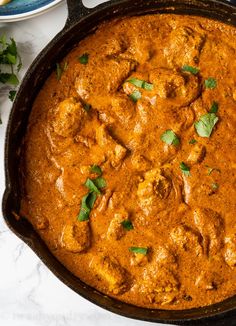 a skillet filled with chicken curry and garnished with cilantro leaves