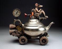 a silver teapot with an animal sitting on it's top and two clocks