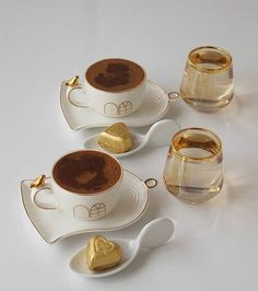 there are four cups and spoons with gold hearts in them on the white table