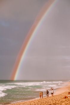 a rainbow appears over the ocean as people walk on the beach