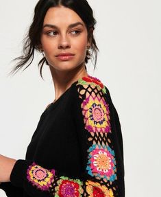 a woman wearing a black sweater with colorful crochet on it