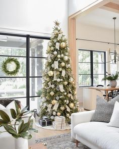 a decorated christmas tree in a living room with white and gold ornaments on the top