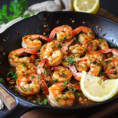 a pan filled with cooked shrimp and garnished with parsley next to a lemon wedge