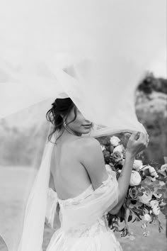 a woman in a wedding dress holding a veil over her head