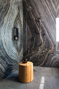 a bathroom with marble walls and flooring in the shower area, along with a wooden stool