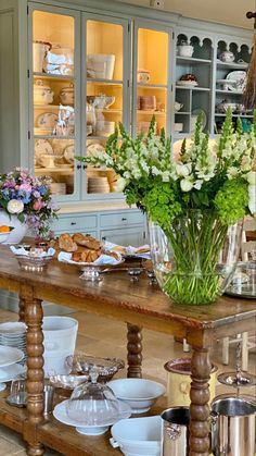 a wooden table topped with lots of plates and vases filled with flowers on top of it