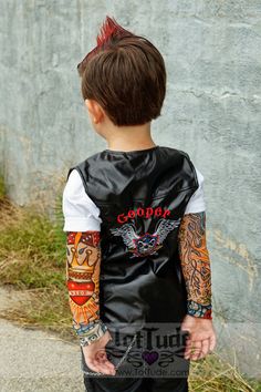 a young boy with tattoos on his arms and arm sleeves, standing in front of a concrete wall