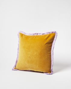 a yellow and purple pillow with ruffled edges sitting on a white surface in front of a plain background