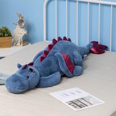 a blue stuffed dragon laying on top of a bed next to a book and toy