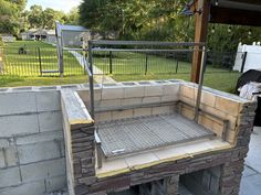 an outdoor grill built into the side of a brick wall in front of a yard