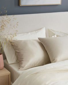 a bed with white sheets and pillows on top of it next to a plant in a vase